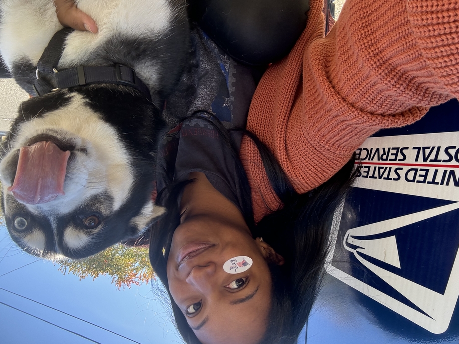 A woman with an I Voted sticker on her cheek posing with her dog