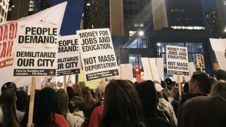 Protestors holding signs that say "People Demand - Demilitarize Our City"