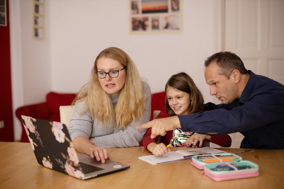 A mother and father teaching their child something on a computer