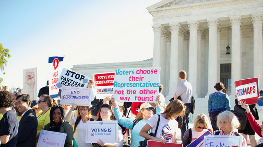 Rally participants stand in front of the Supreme Court with signs demanding fair maps