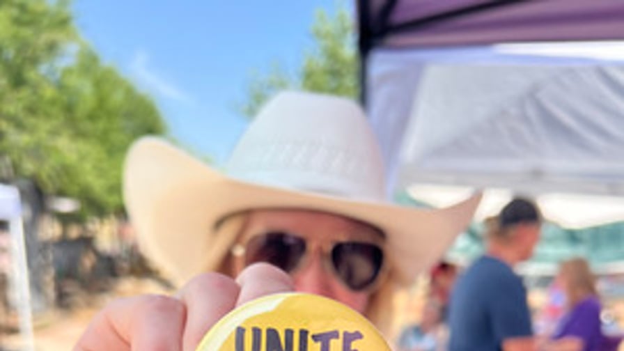 A person in a cowboy hat holding a "Unite and Rise" pin
