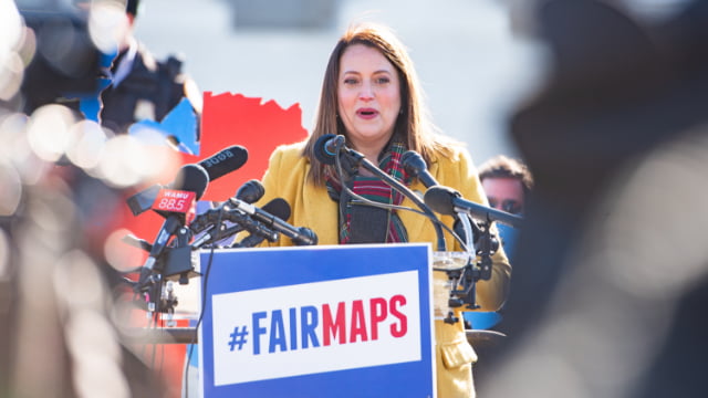 Virginia Kase stands behind a Fair Maps sign